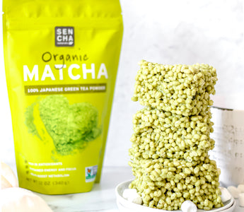 Photo of a bag of Sencha Naturals Matcha green tea powder next to a stack of 3 rice krispies treats squares on a white plate, with a few small marshmallows strewn about, all on a white background